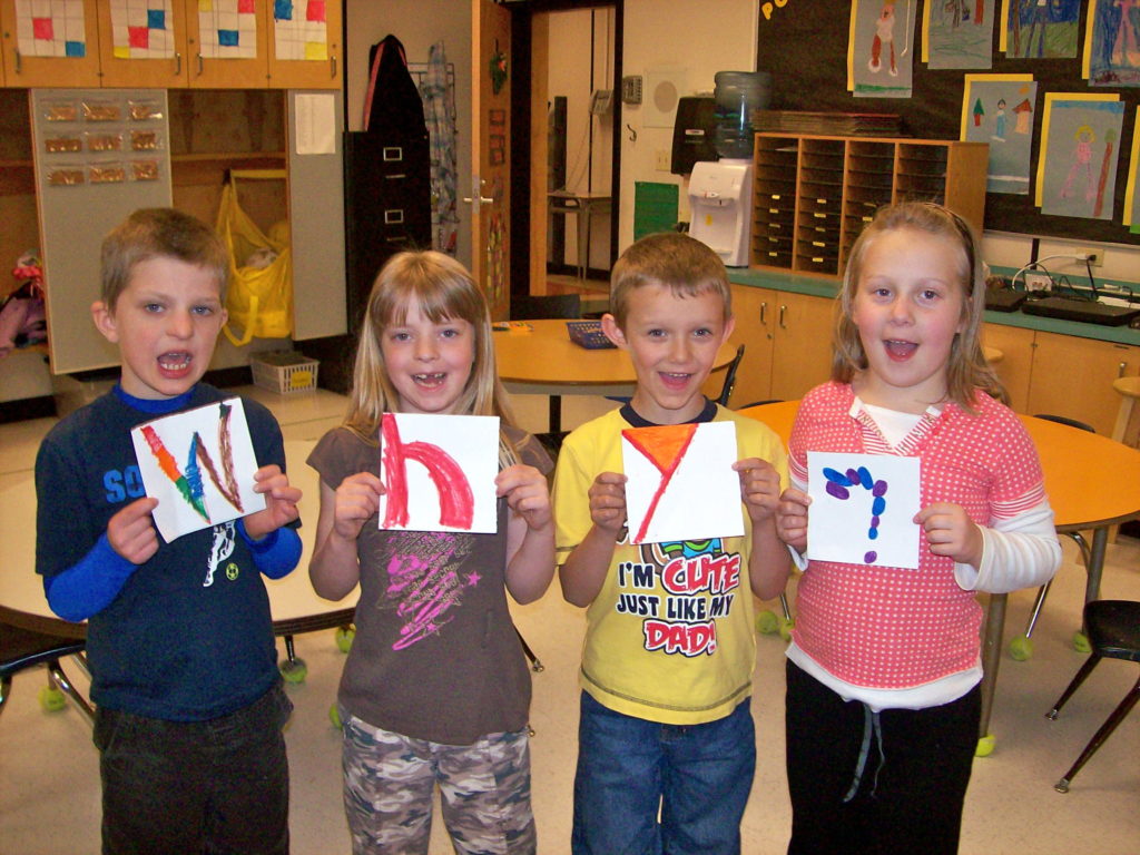Four children each holding one letter on a square piece of paper that spells Why?