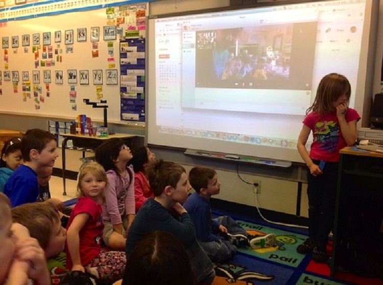 Students using technology in classroom by video conferencing with another class.