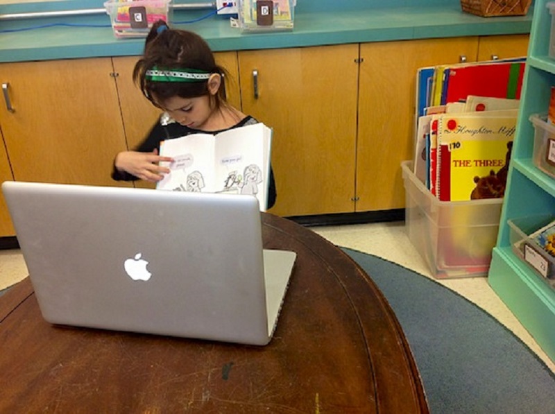 Elementary student sitting at a table in front of a computer preparting to blog.